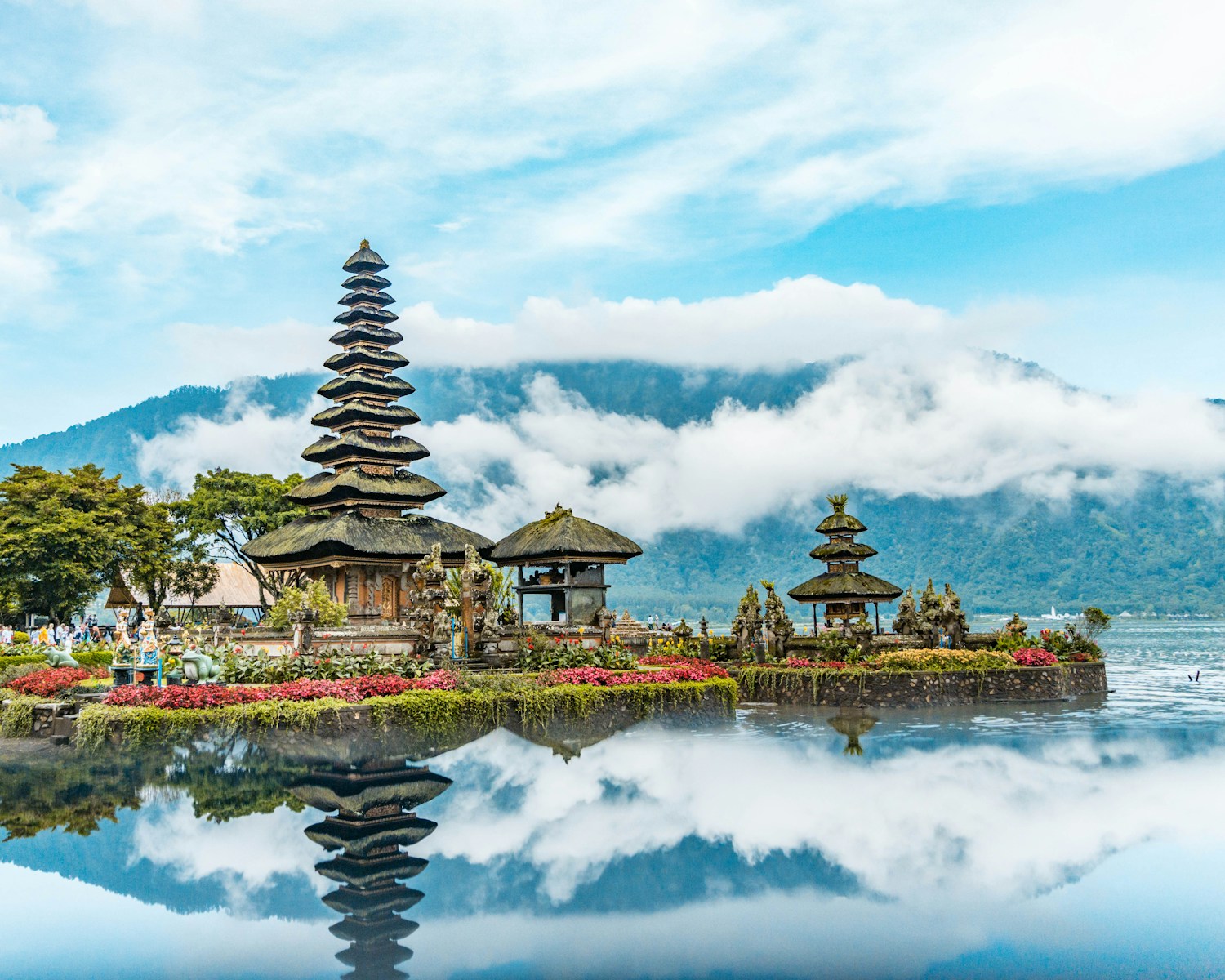 brown and green temple near body of water under blue and white cloudy sky during daytime